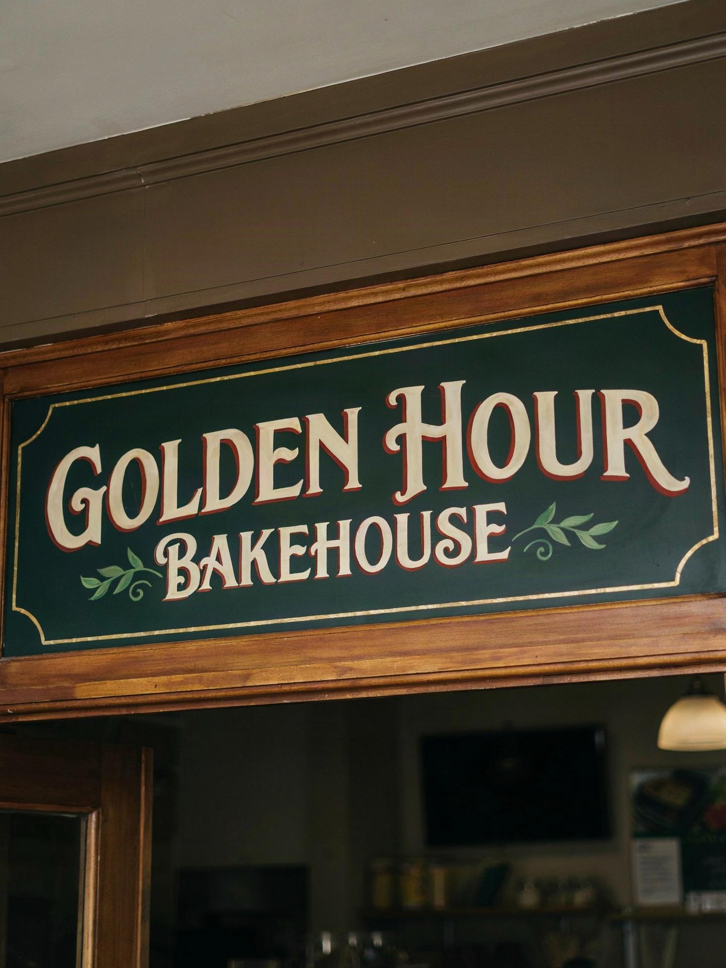 A hand-painted bakery shop sign in cream serif lettering on deep green