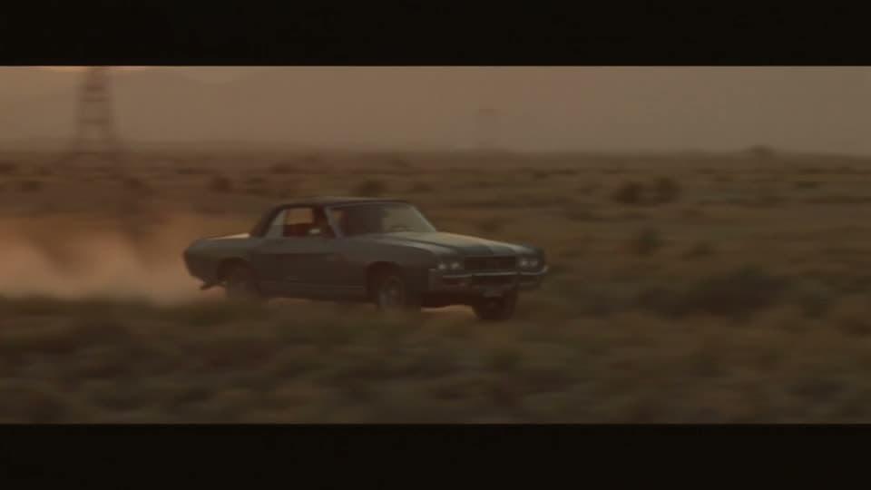A vintage convertible cresting a desert ridge at sunset