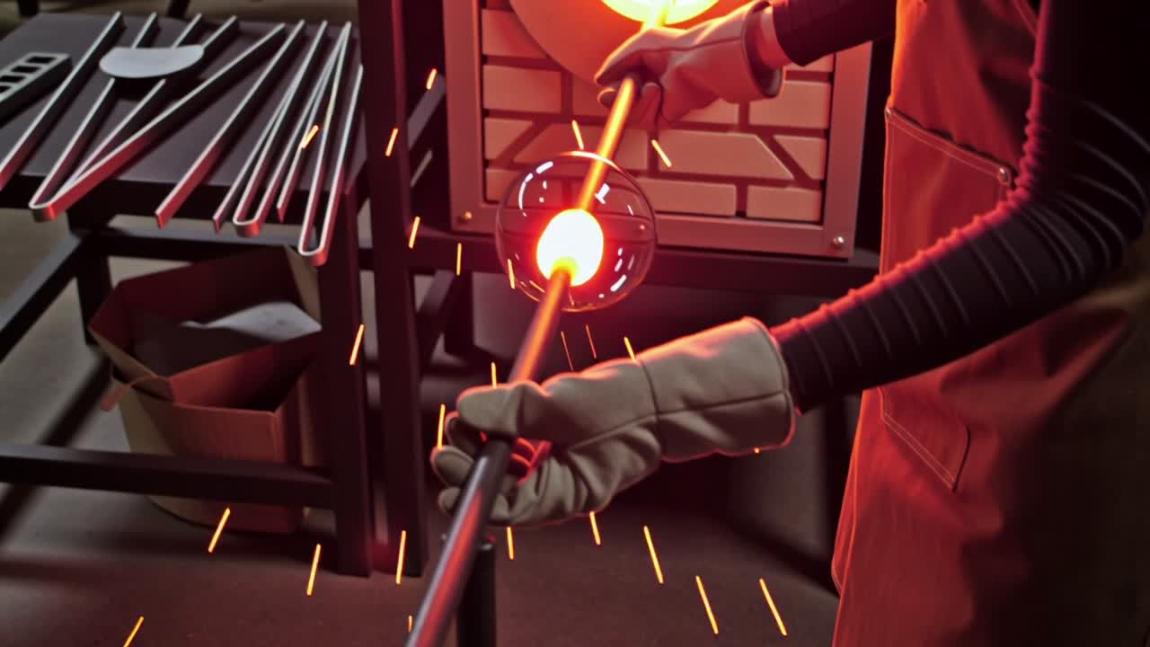 A glassblower turning a molten gather at the furnace mouth