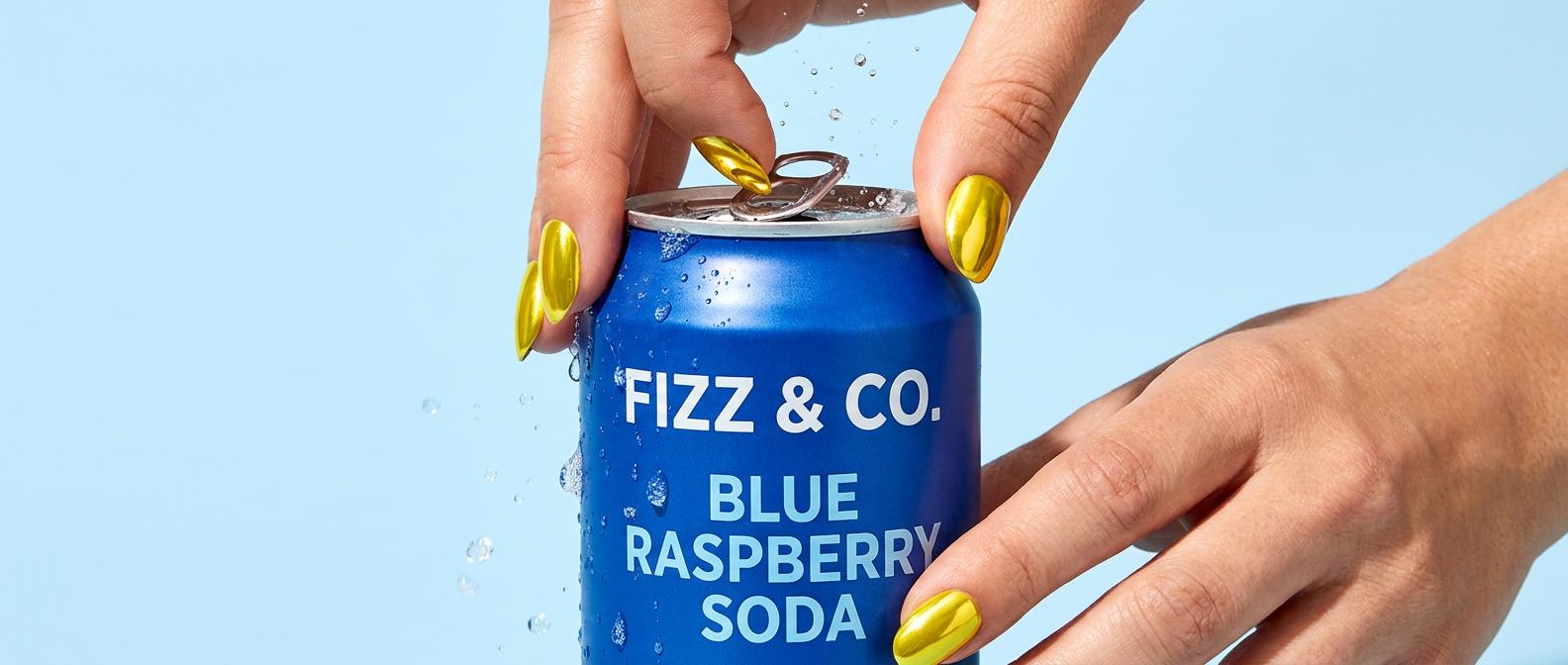 Hands with chrome-yellow nails opening a cobalt-blue soda can labeled Fizz and Co Blue Raspberry Soda