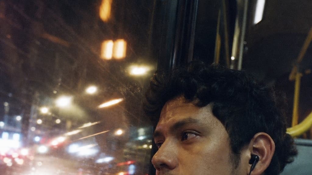 A young man rides a city bus at night, the lit street motion-streaked across the window — made with GPT Image 2 Medium.