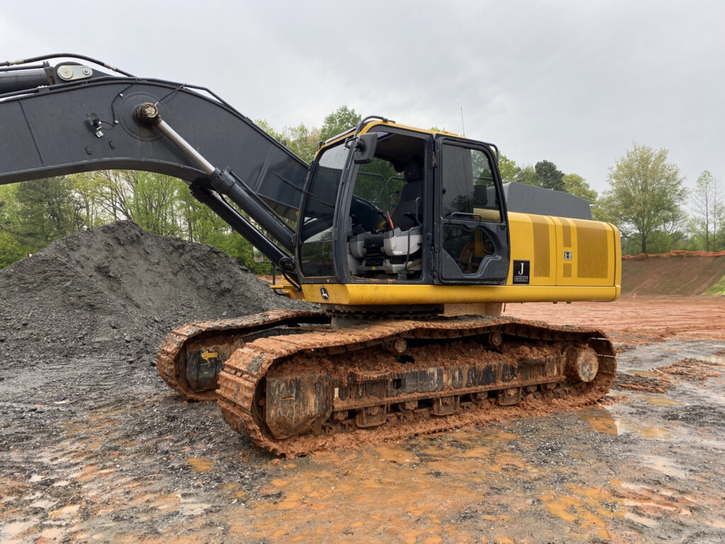 John Deere excavator on a muddy construction site with tinted cab windows