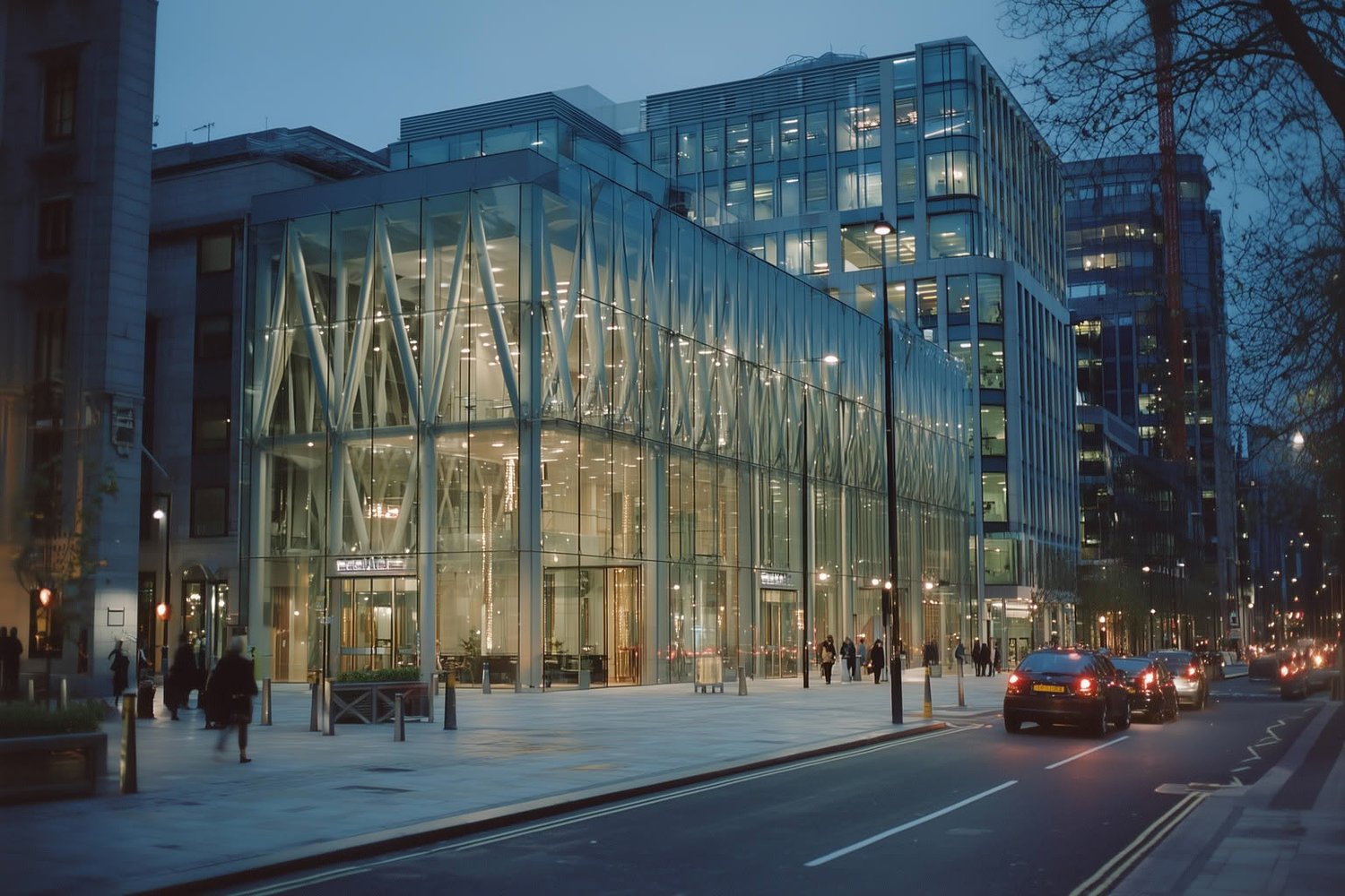 Modern glass office buildings at dusk with internal lights glowing on an urban street.