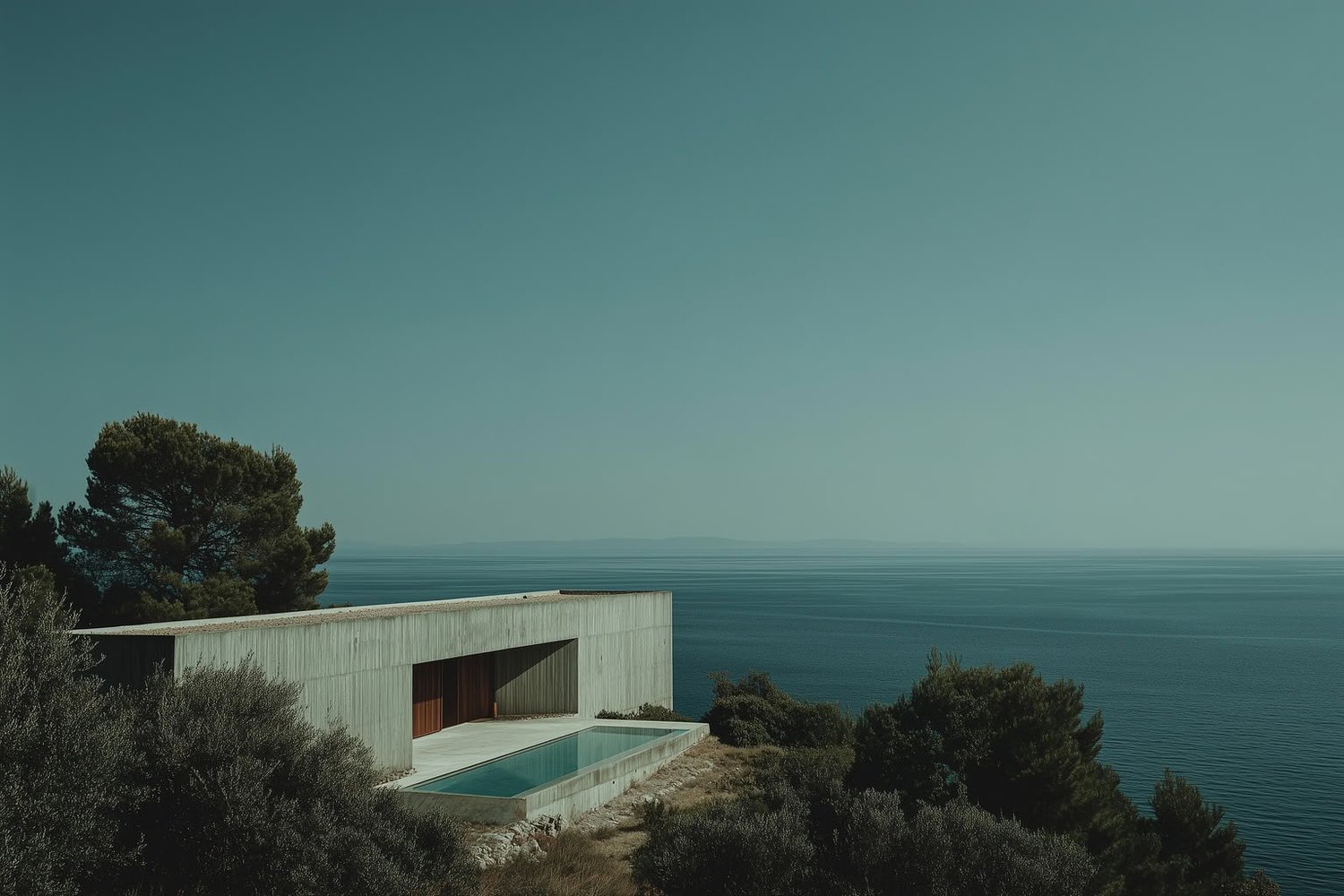 Modern minimalist concrete house with infinity pool overlooking a calm blue sea.