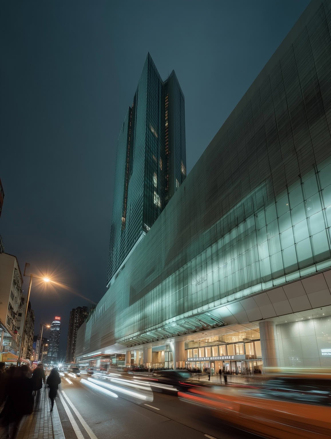 Night view of a modern city street with tall glass buildings, blurred car lights, and pedestrians.