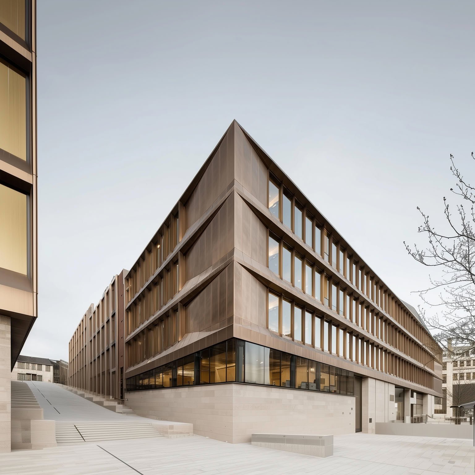 Sharp-angled modern building with warm bronze panels and a grand stone plaza.