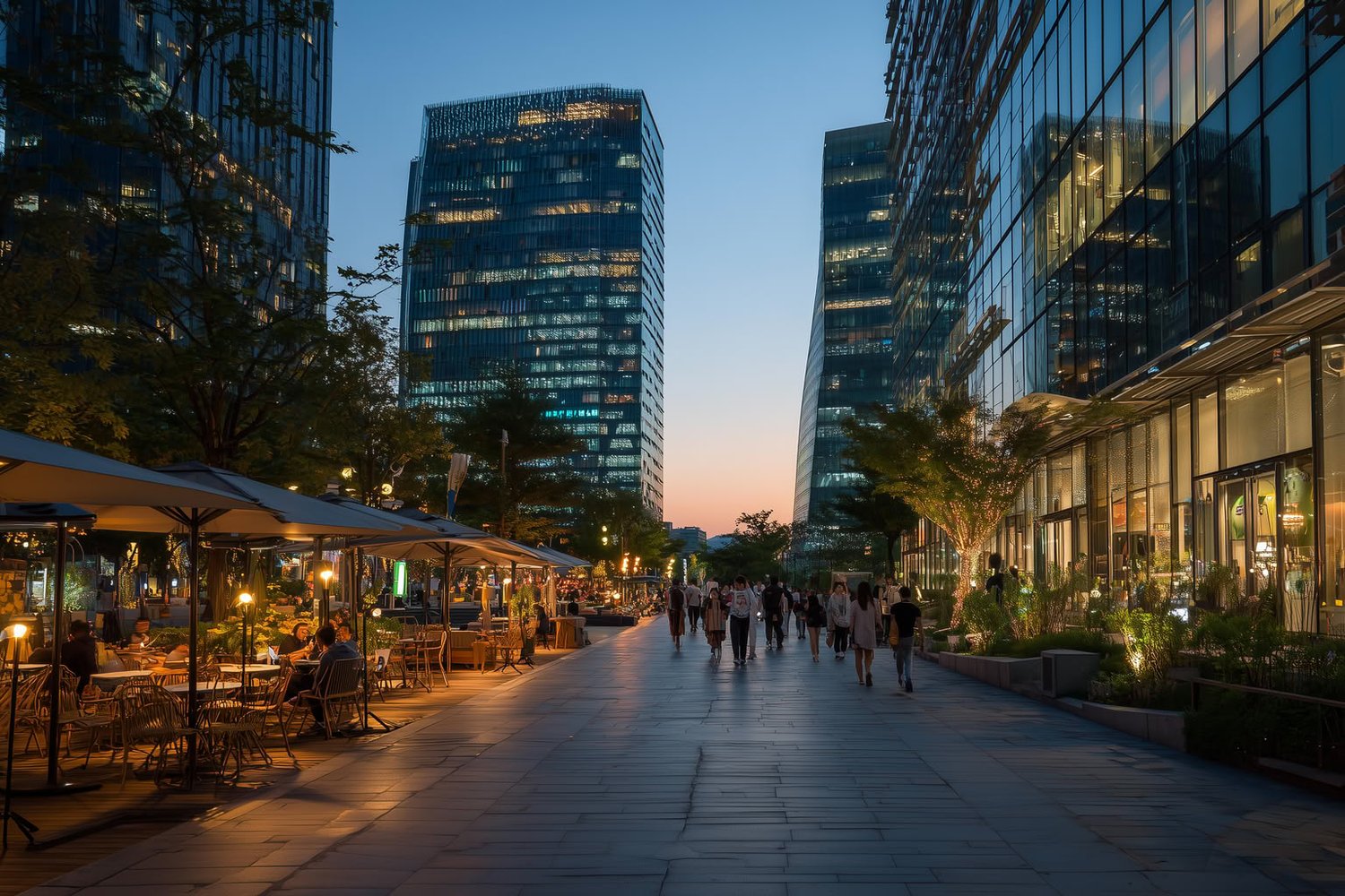 Modern glass buildings frame a pedestrian street with illuminated outdoor cafes at dusk.