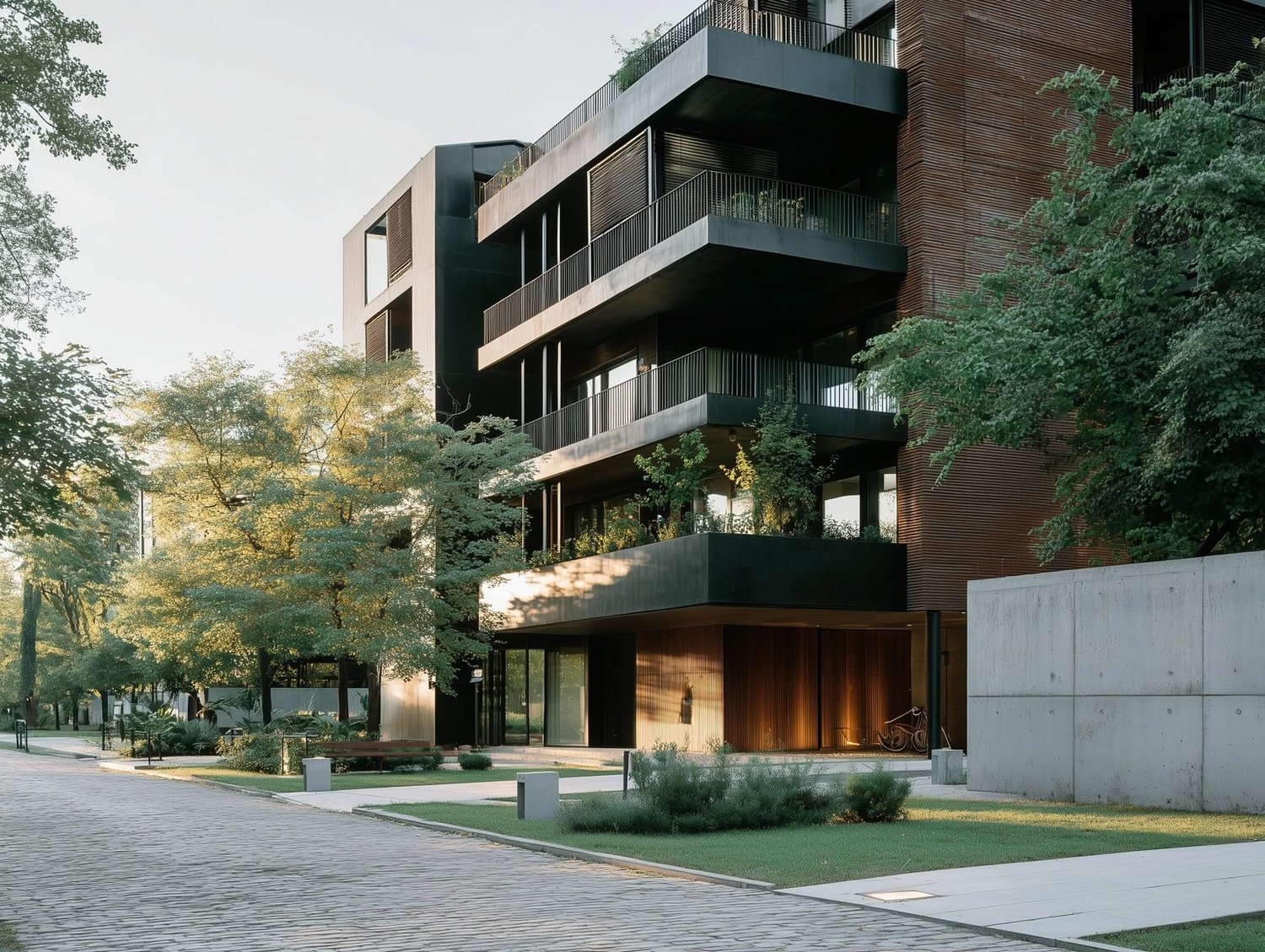 Modern building with dark balconies, wood cladding, lush trees, and a paved path under soft sunlight.