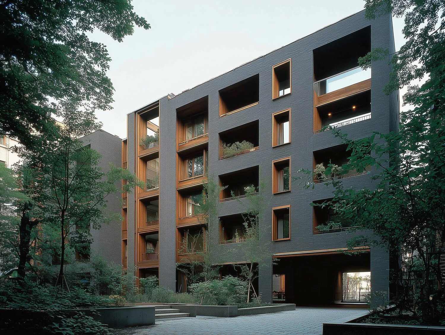 A modern building with dark grey textured facades, warm wood windows and balconies, and lush surrounding trees.