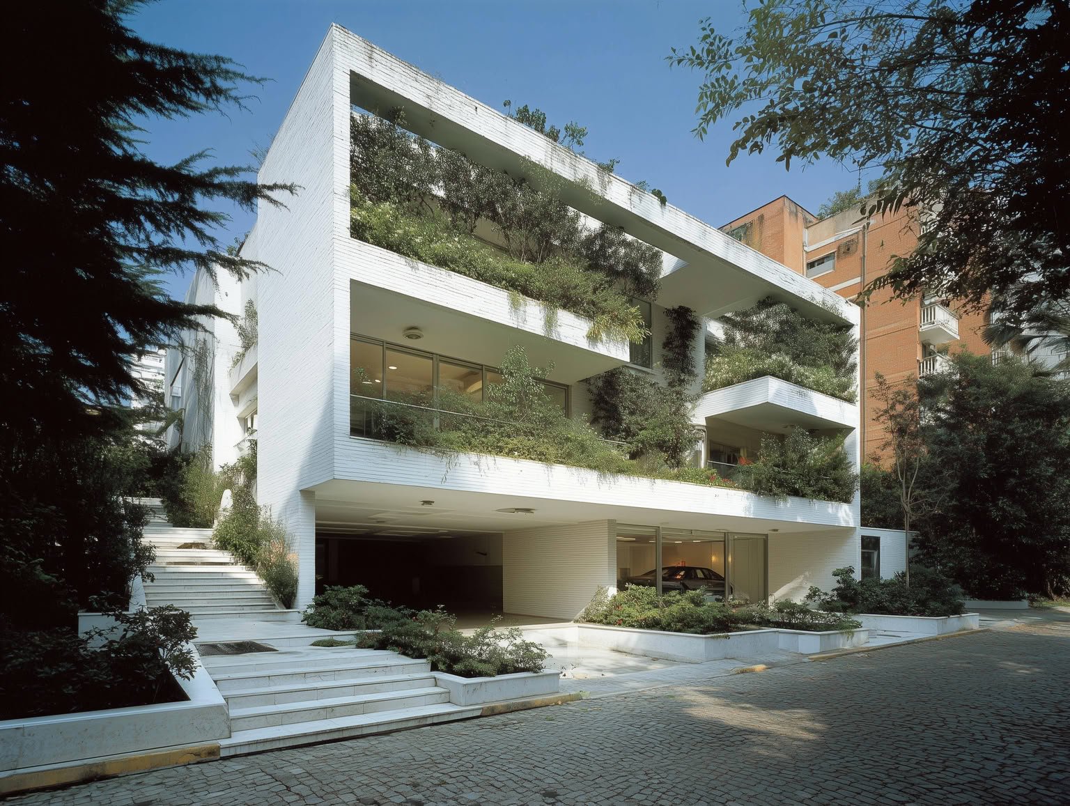 A modern white building with multiple plant-filled balconies and a clear blue sky.