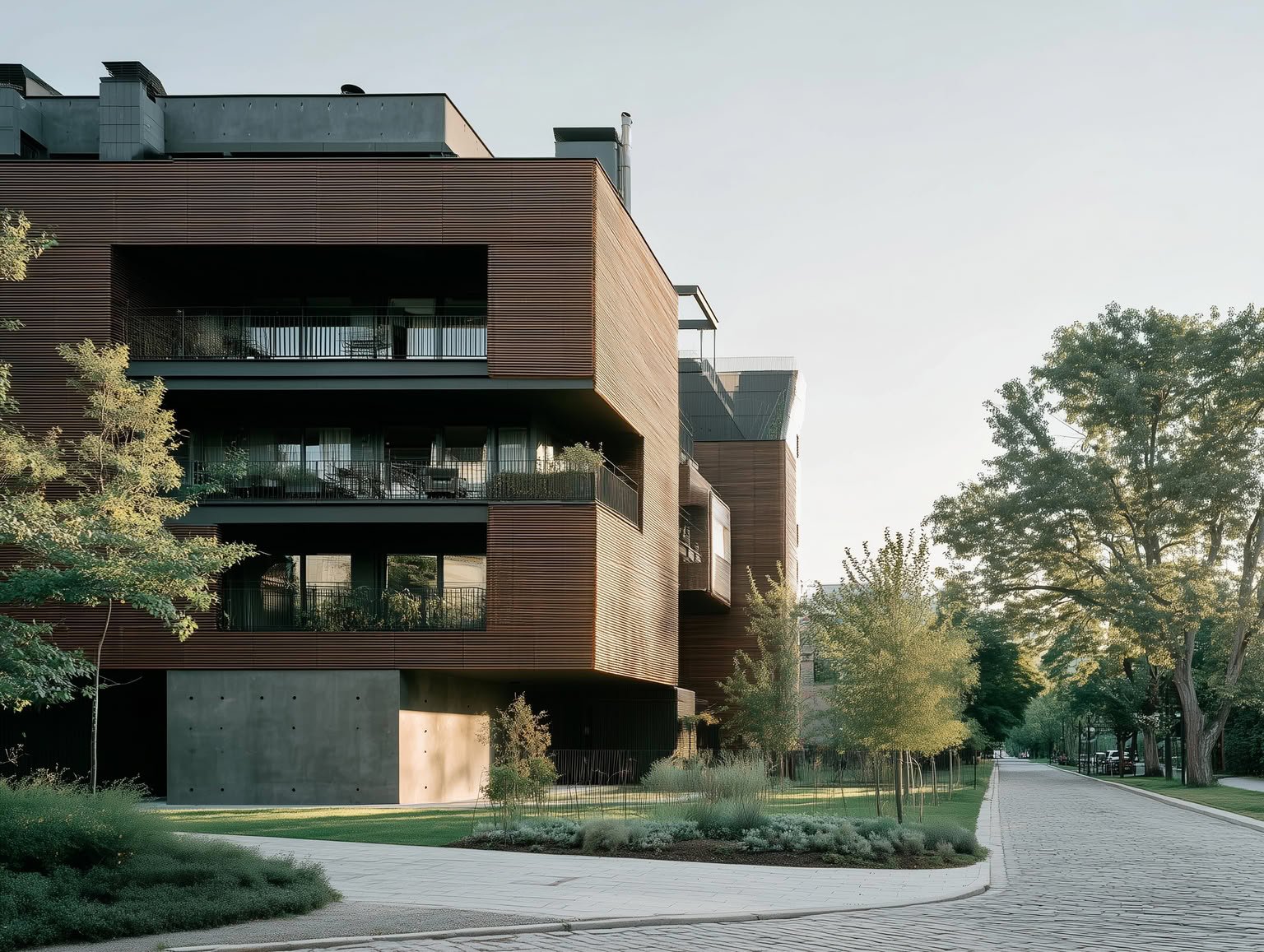 Modern building with warm wooden slat cladding, dark balconies, large glass windows, and concrete base next to a cobblestone path and trees.