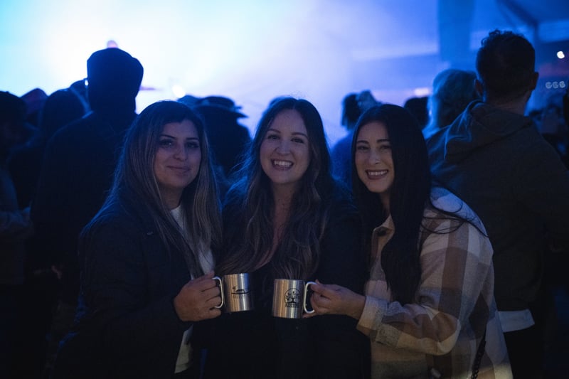Three friends holding mugs at Harvest Party 2024.