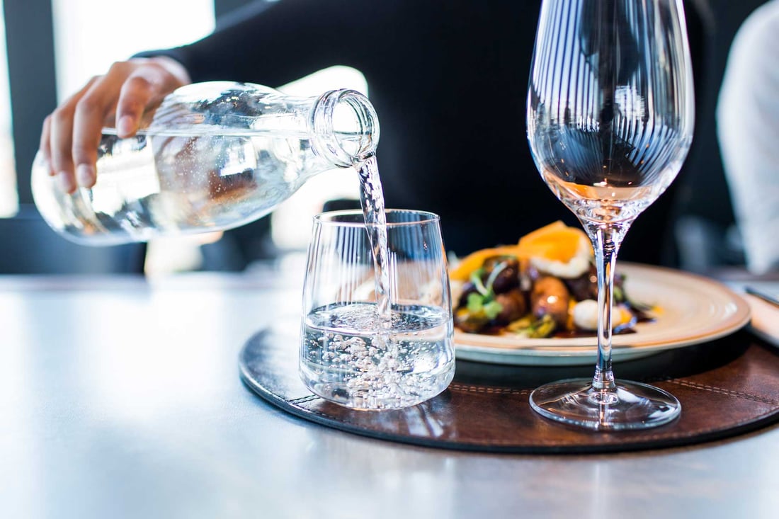 Gefiltertes Wasser wird am gedeckten Tisch aus einer Glaskaraffe eingeschenkt