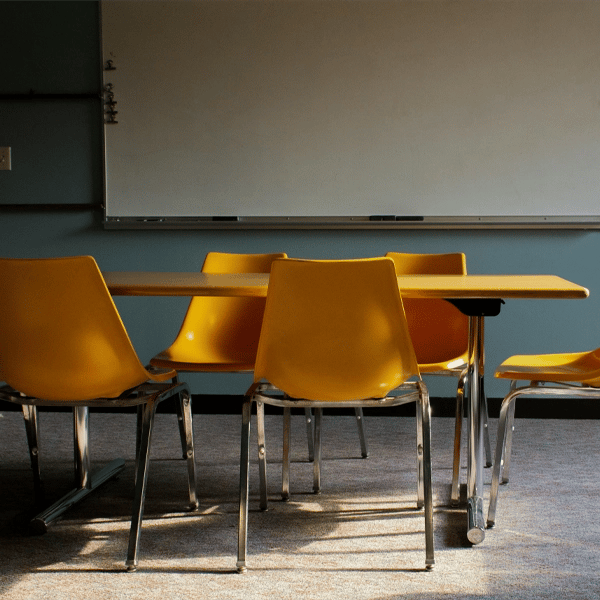 Empty classroom with yellow chairs around a table in front of a whiteboard