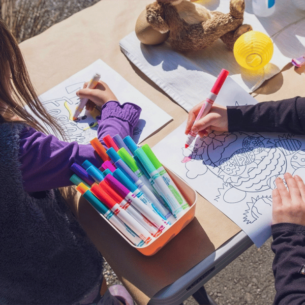 Two children coloring on printed education posters with markers at a table