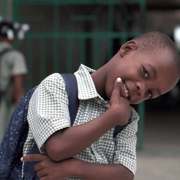 Smiling young student in school uniform with a backpack, posing playfully outside a school building