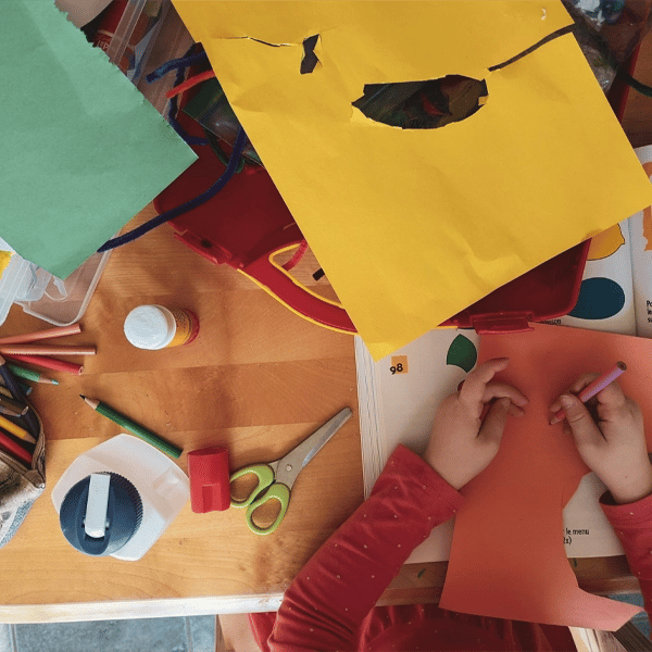 Blog Post 10.9.2 Child working with colored paper, scissors, and art supplies at a desk, creating a poster for classroom learning