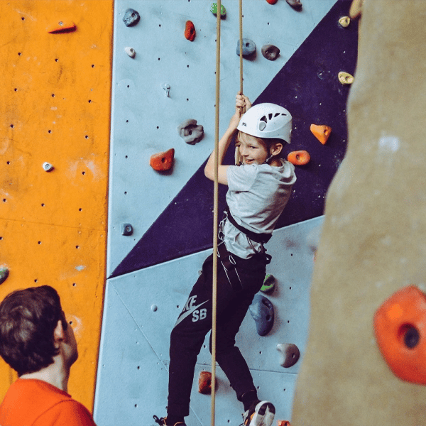 Child rock climbing on an indoor wall during a school event, guided by an instructor