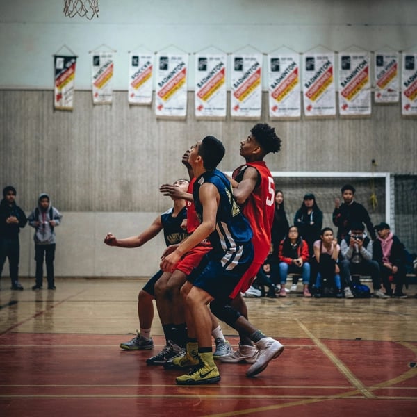 A high school basketball game in progress with players in blue and red jerseys competing near the hoop, showcasing athletic action and school sports spirit