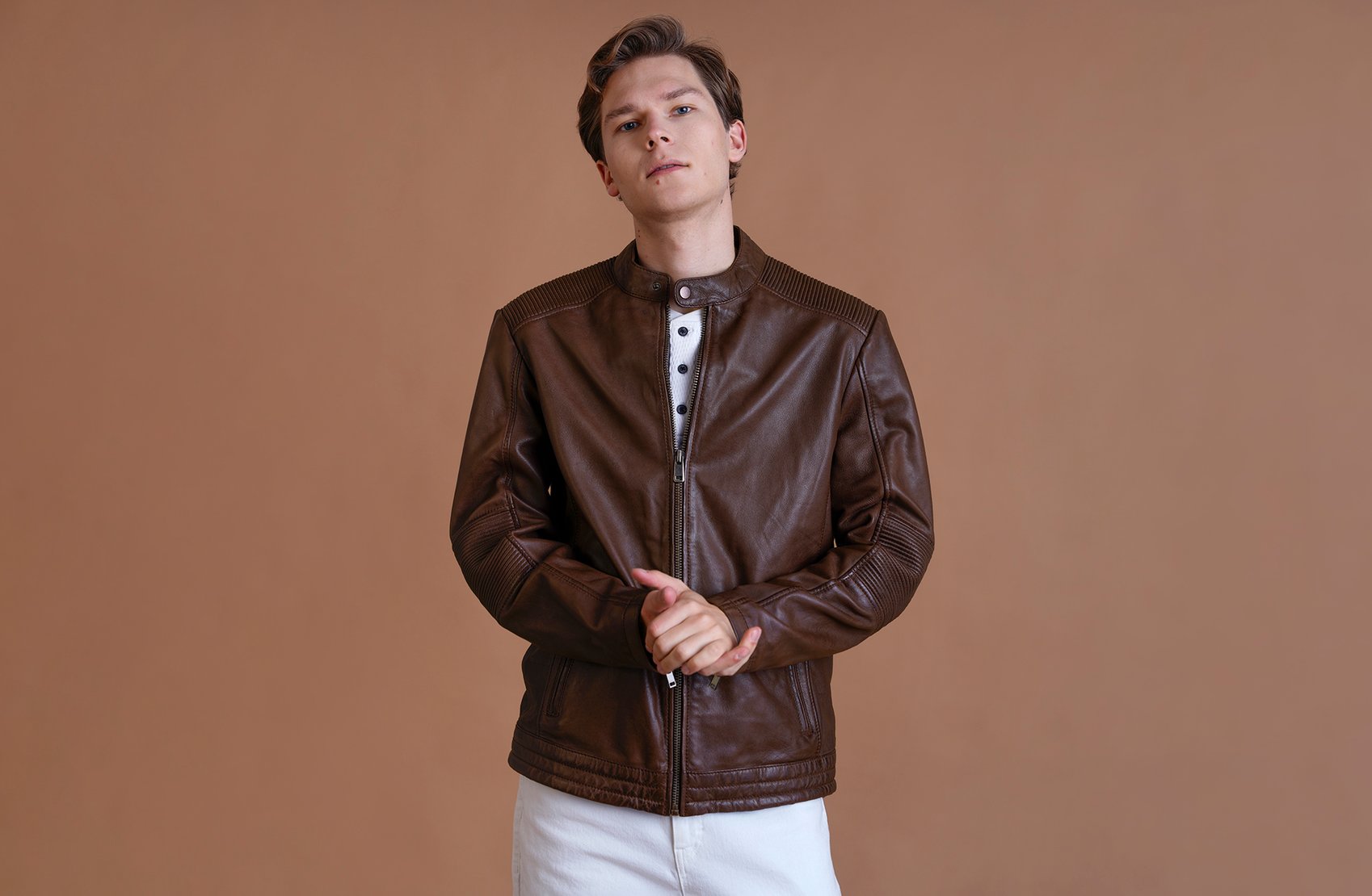 A man styling a brown leather jacket over a shirt and chinos, demonstrating layered utility.