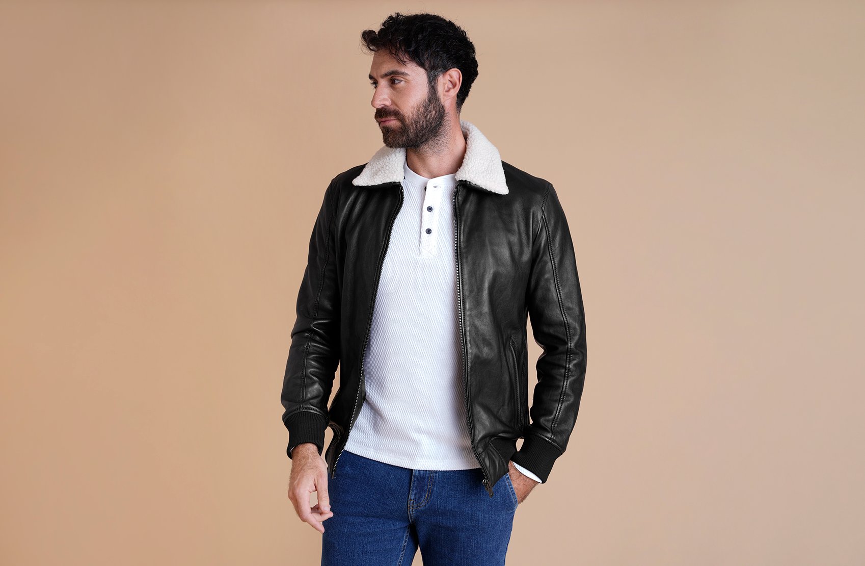 A man wearing a black leather jacket with a detachable shearling/borg collar in a street setting.