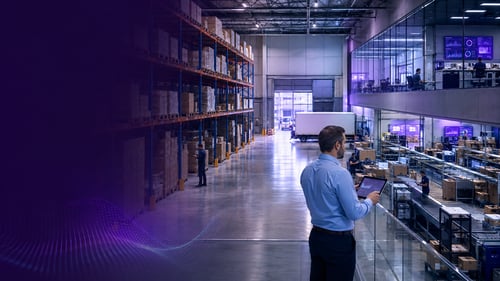 almacén logístico con estanterías de palets y un responsable consultando una tableta frente a las oficinas acristaladas y la línea de preparación de pedidos, gestionado con los erps sectoriales de galdón software