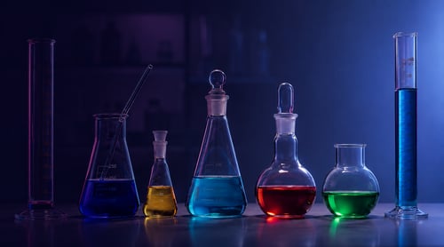 matraces y probetas de laboratorio con líquidos de colores sobre una mesa oscura, gestionados con el erp química y software para laboratorios químicos de galdón software