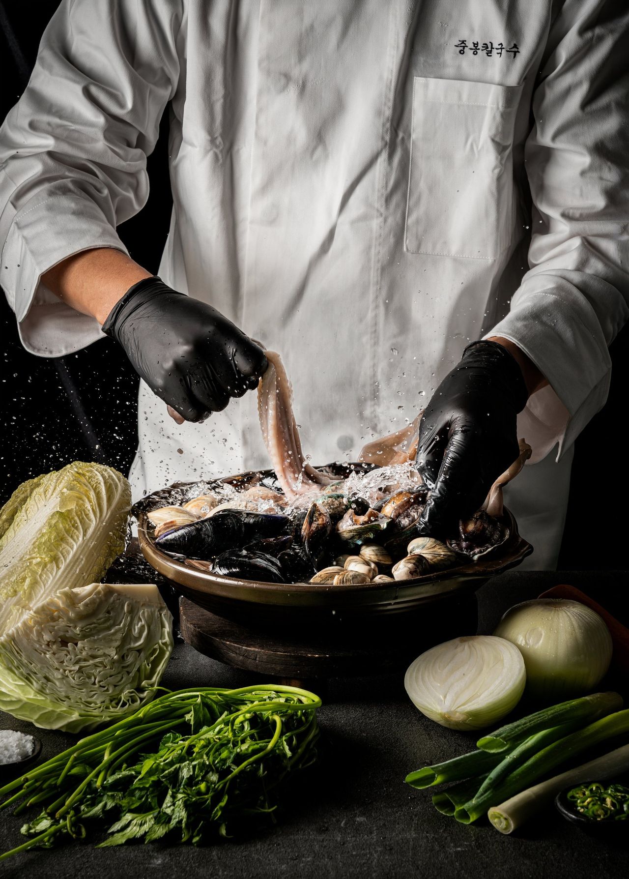 중봉칼국수 포스터 촬영 - 검은 장갑을 낀 손이 해물을 들어 올리며 물이 튀는 셰프 무드컷