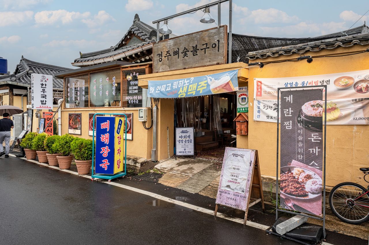 경주뼈숯불구이 인테리어 촬영 - 기와지붕 아래 나무 현판과 초록 화분이 놓인 한옥 매장 주간 외관