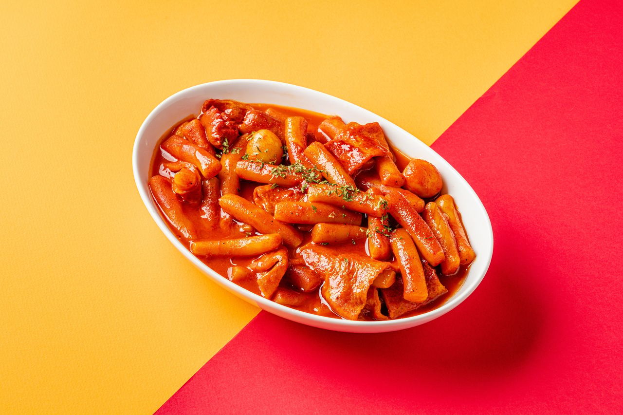 요용떡볶이 배달음식 촬영 - 노랑·빨강 사선 2색 배경 위 흰 타원 접시의 떡볶이 단품