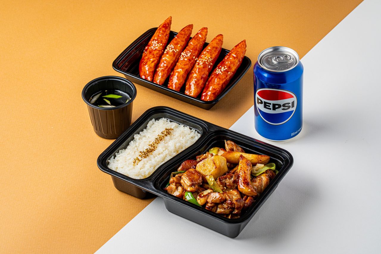 인천 주안 치킨 배달 촬영 - 닭고기 볶음 도시락과 양념 스틱 용기, 국물 컵, 캔 음료를 함께 놓은 1인 세트