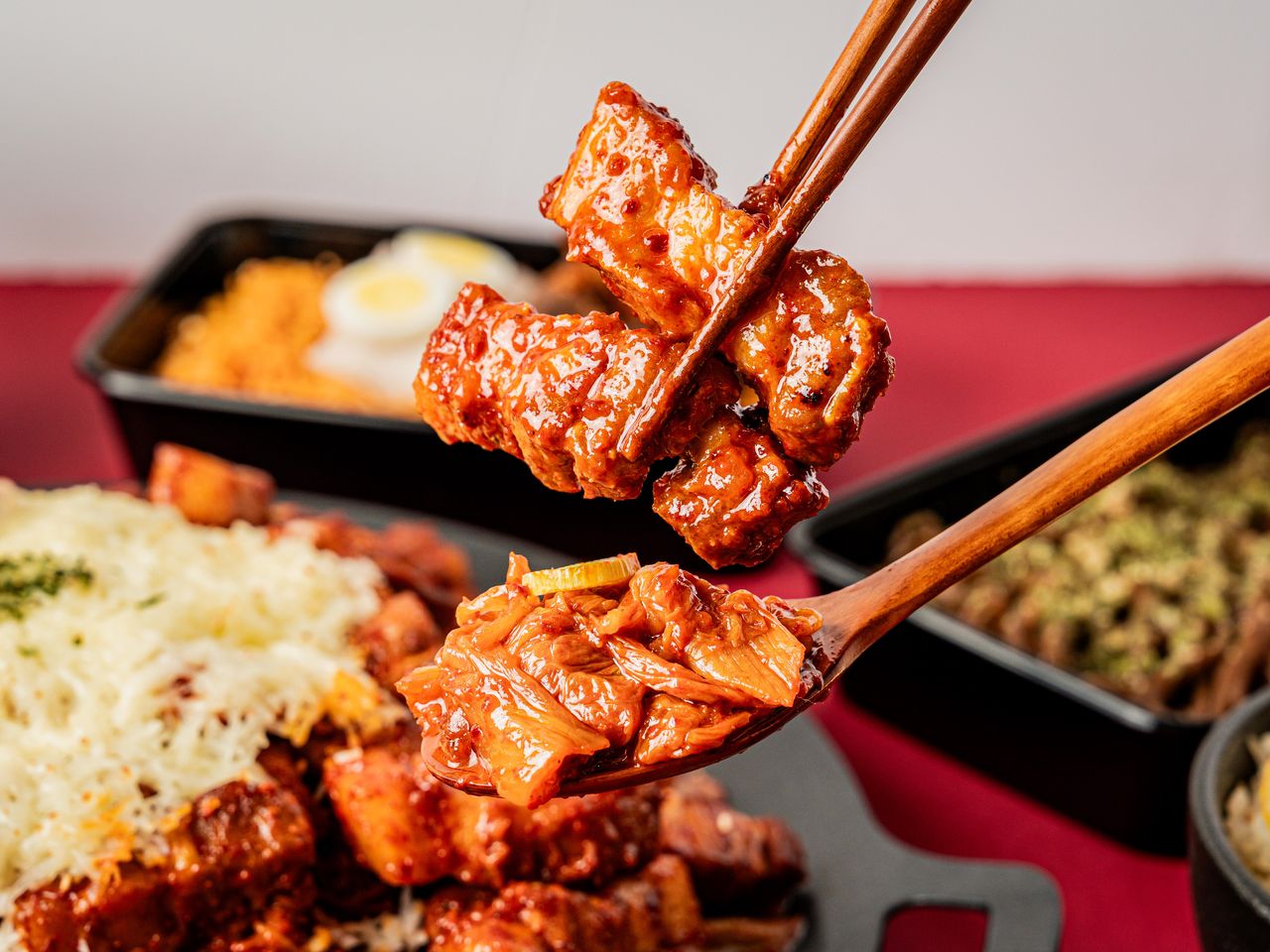 수유 배달 한식 메뉴사진 촬영 - 젓가락으로 든 양념 삼겹살과 나무 숟가락 위 볶은 김치, 앞쪽 치즈 팬과 뒤쪽 면 용기가 흐리게 깔린 시즐컷
