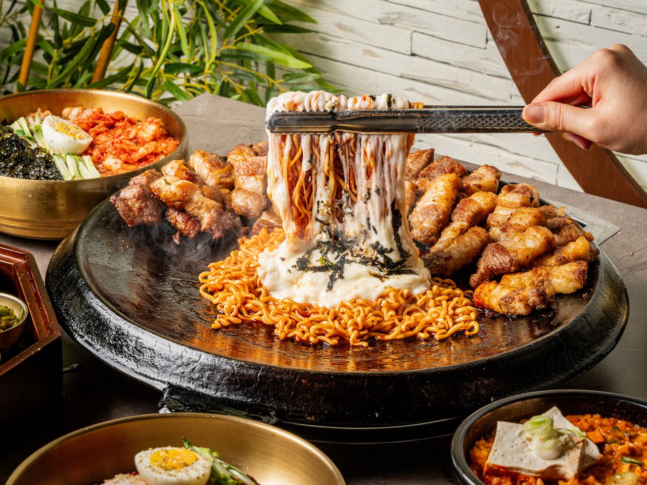고기집 출장 음식사진 촬영 - 김이 오르는 불판에서 집게로 치즈 볶음면을 들어 올려 치즈가 늘어나는 순간