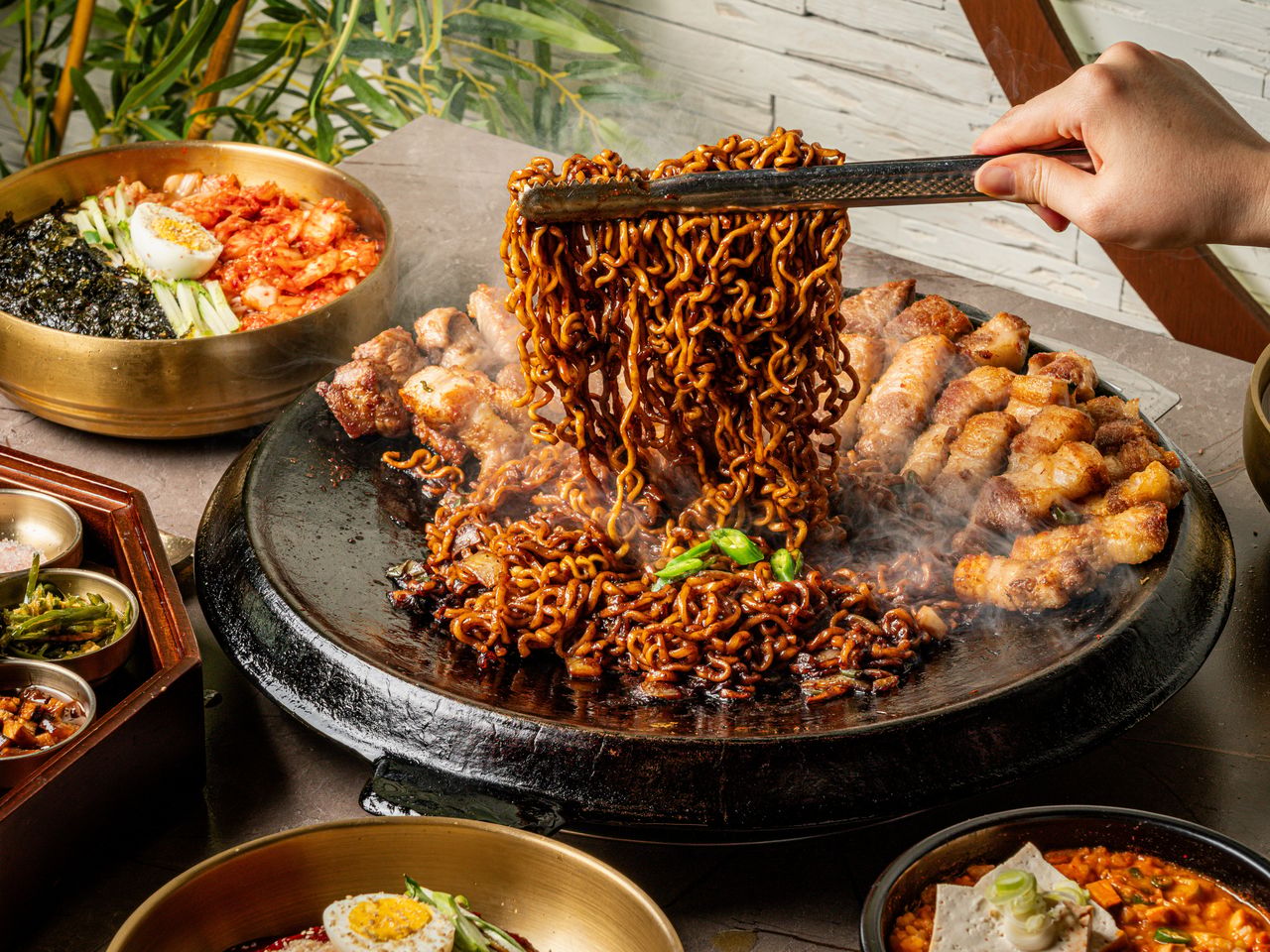 고기집 출장 음식사진 촬영 - 구운 고기 사이에서 짜장빛 볶음면을 집게로 높이 들어 올린 컷