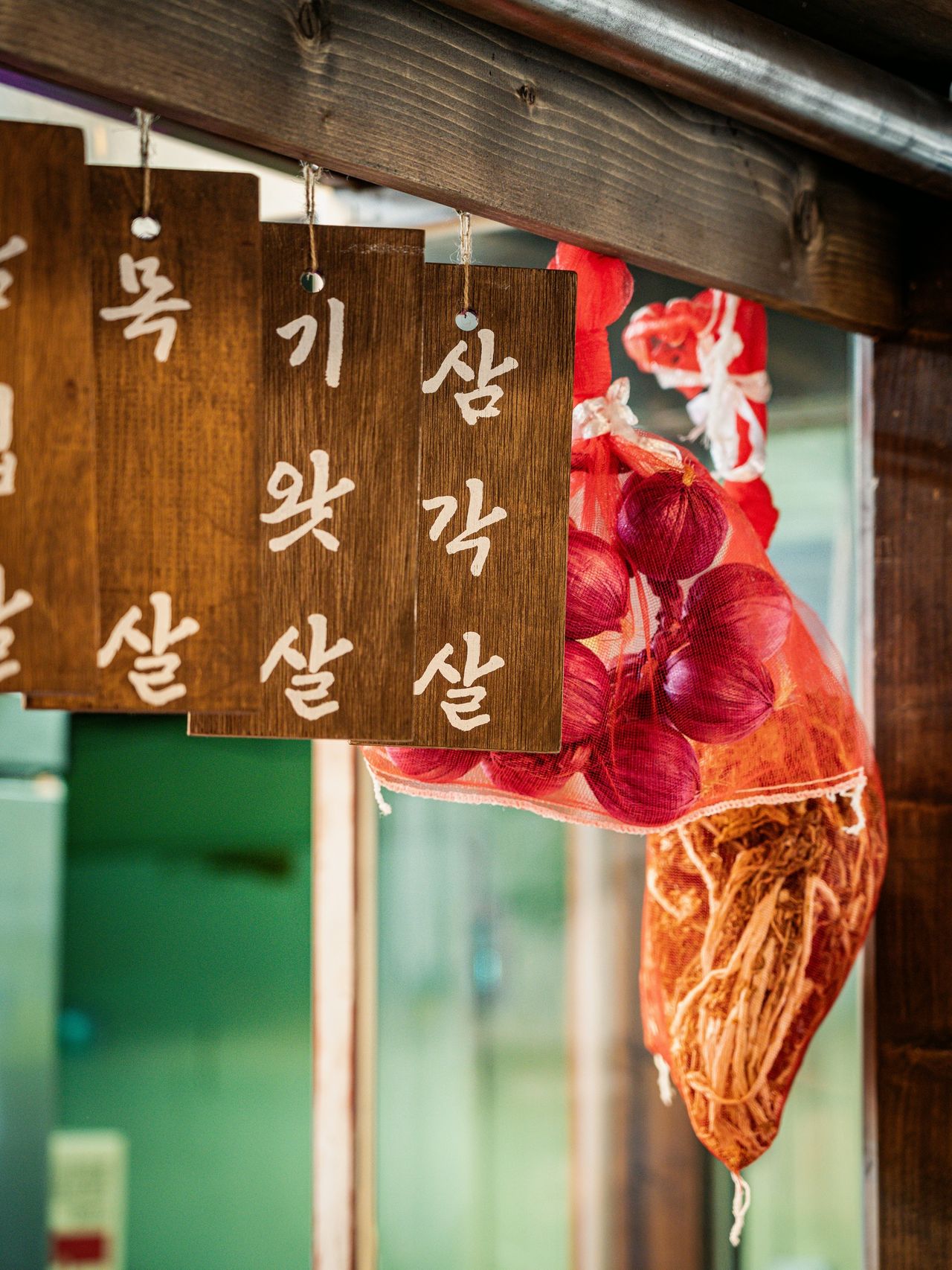 산솔 신사본점 매장 사진 촬영 - 나무 메뉴패 목살·기왓살·삼각살 뒤로 붉은 망에 담긴 자색 양파가 매달린 세로 클로즈업