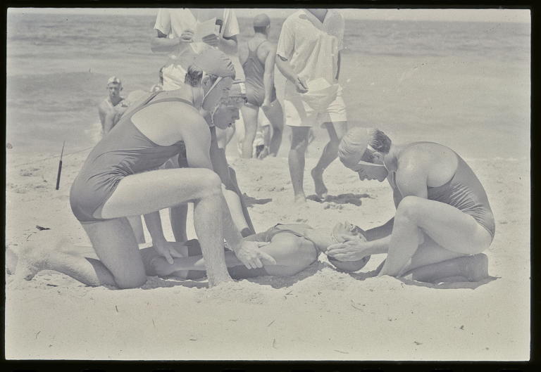 Negative of surf lifesavers practising resuscitation on the beach photographed by David Mist