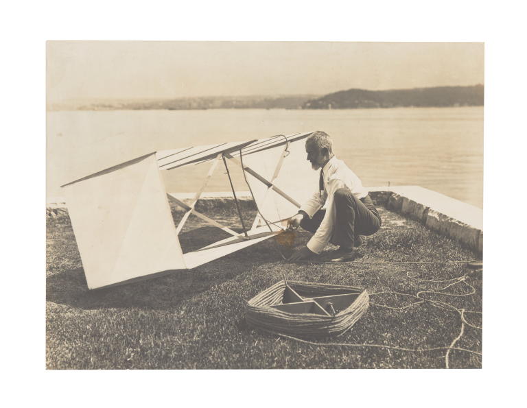 Photograph of Lawrence Hargrave kneeling beside box kite at Woollahra Point