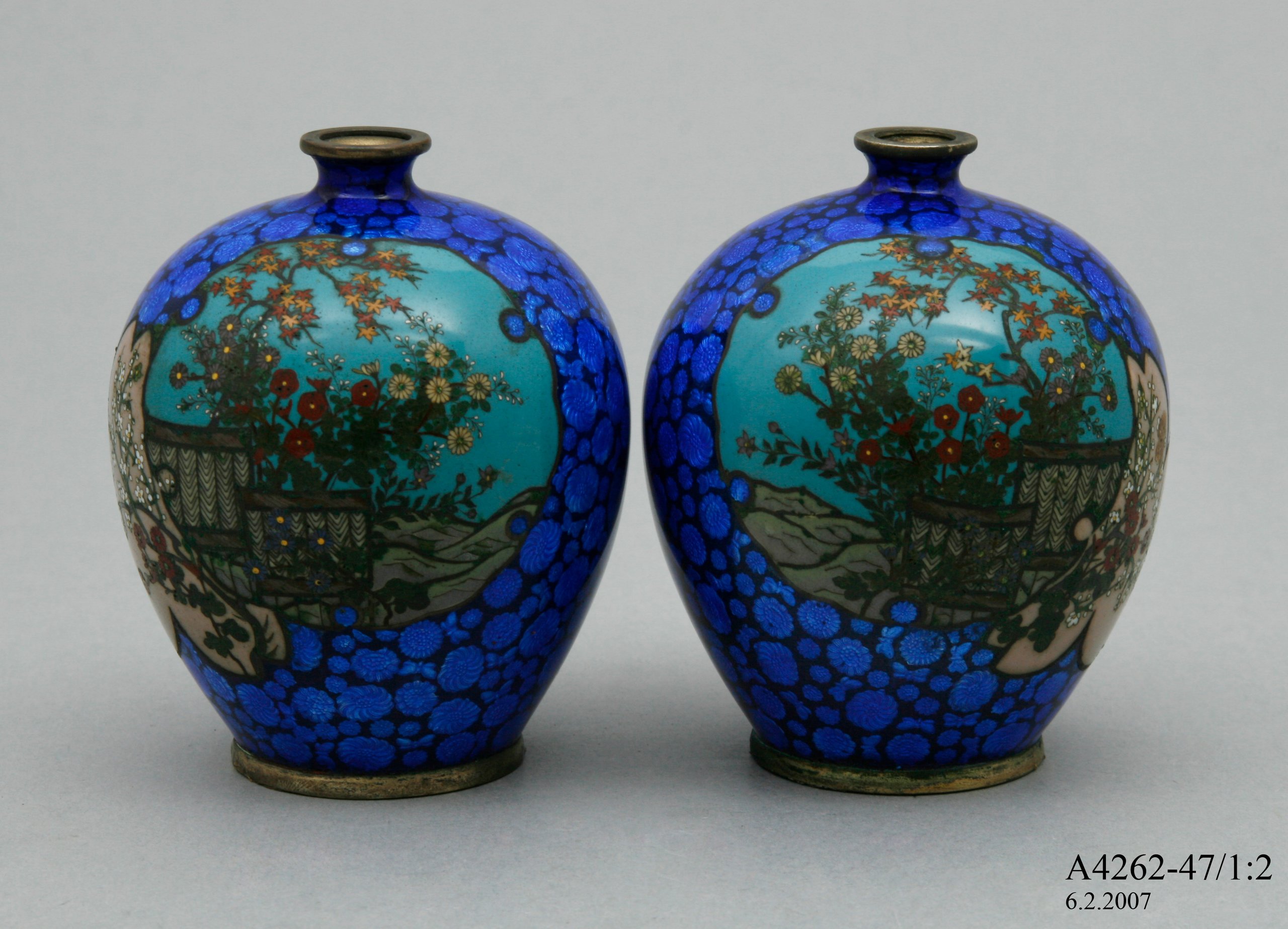 Two cloisonne vases each featuring a landscape scene.