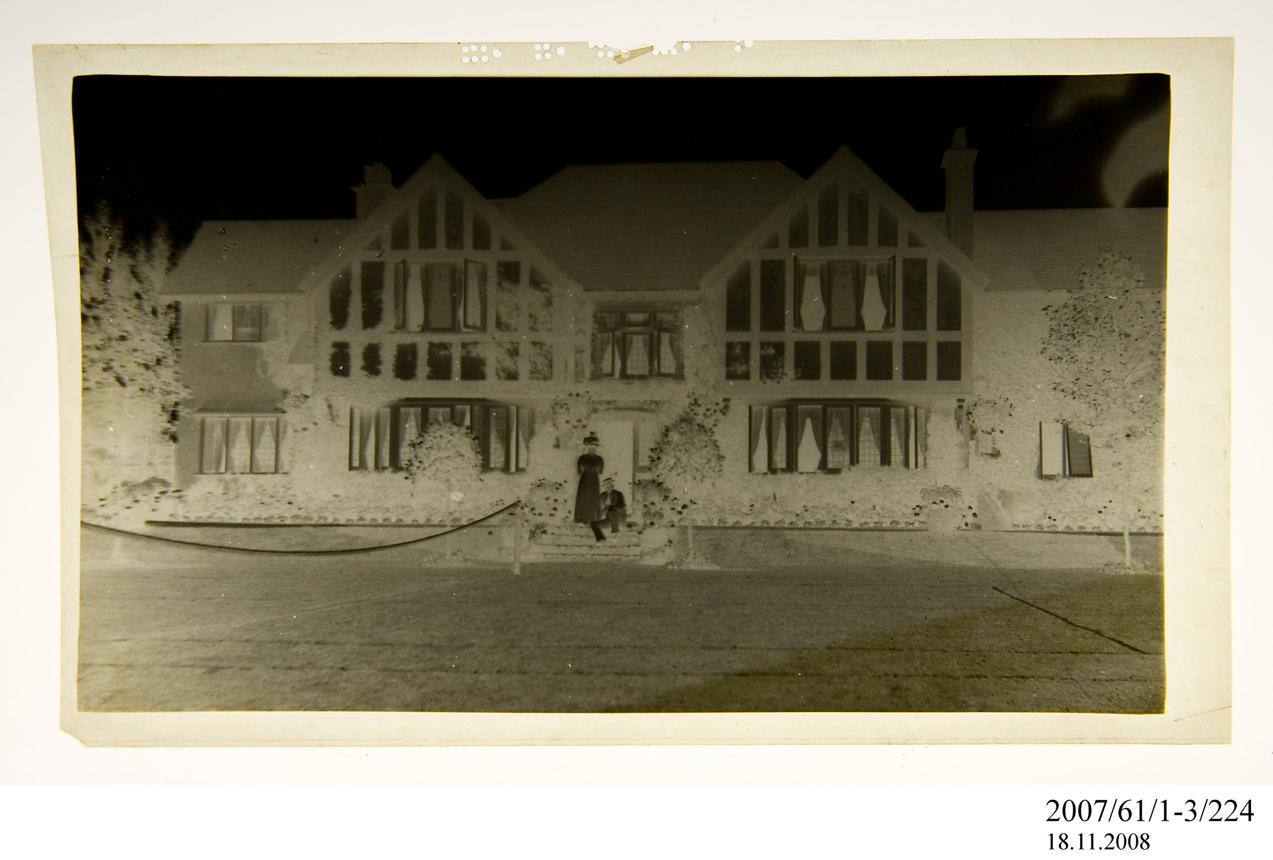 Negative of two people standing near doorway of house