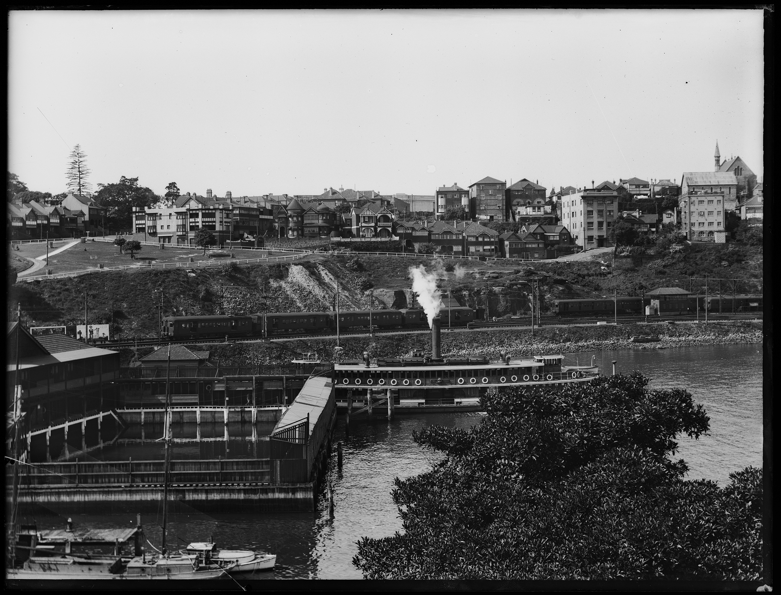 Glass plate negative of steam ferry 'Kulgoa' at ferry wharf, Lavender Bay, Sydney, and North Shore electric trains, 1932-1935