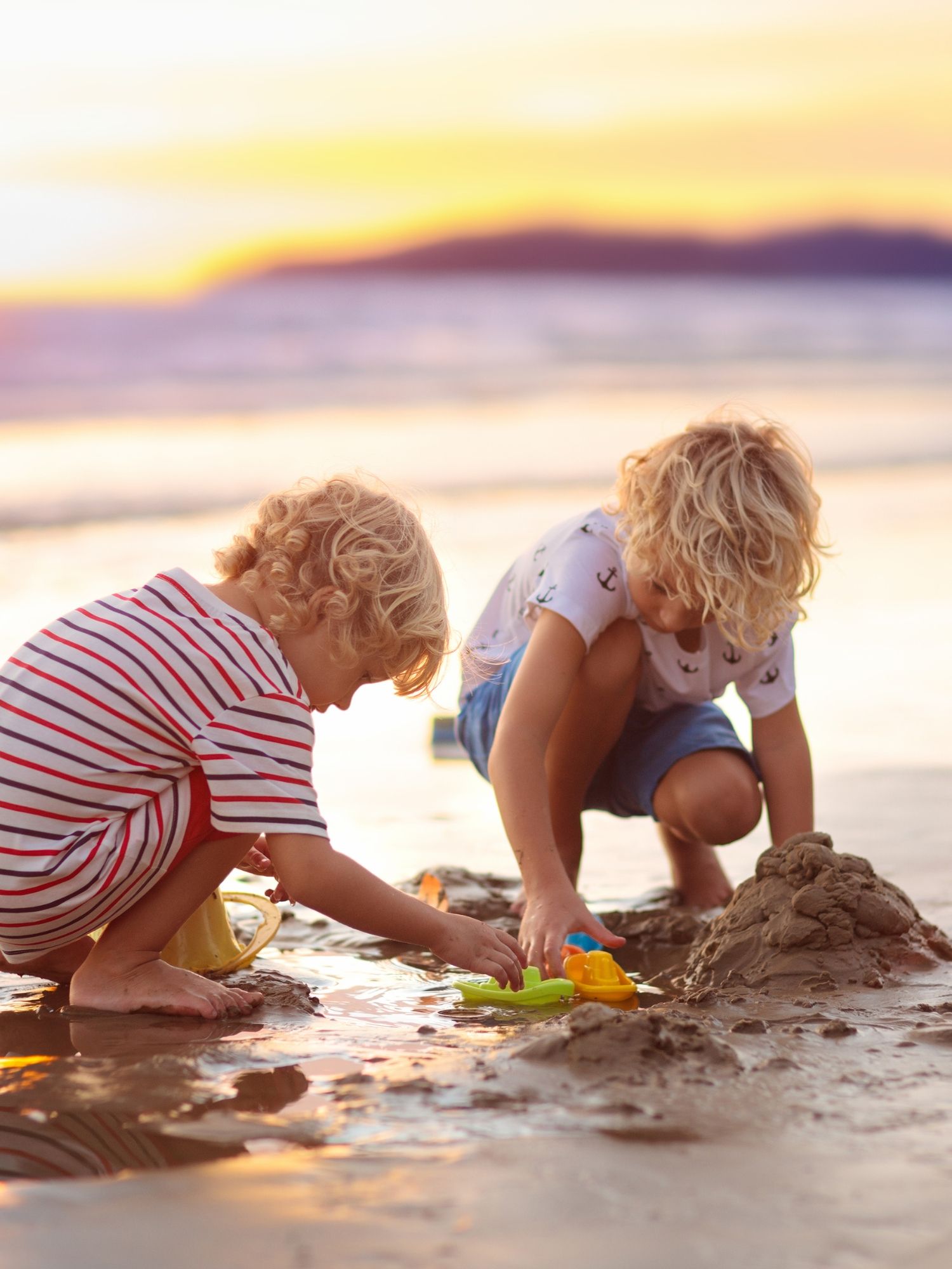 Two children dig in the wet sand at the beach.