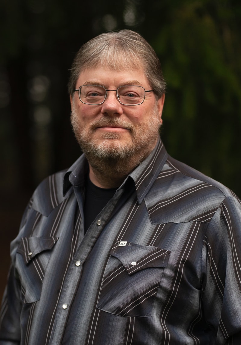 Headshot of a man with glasses and a beard wearing a striped shirt