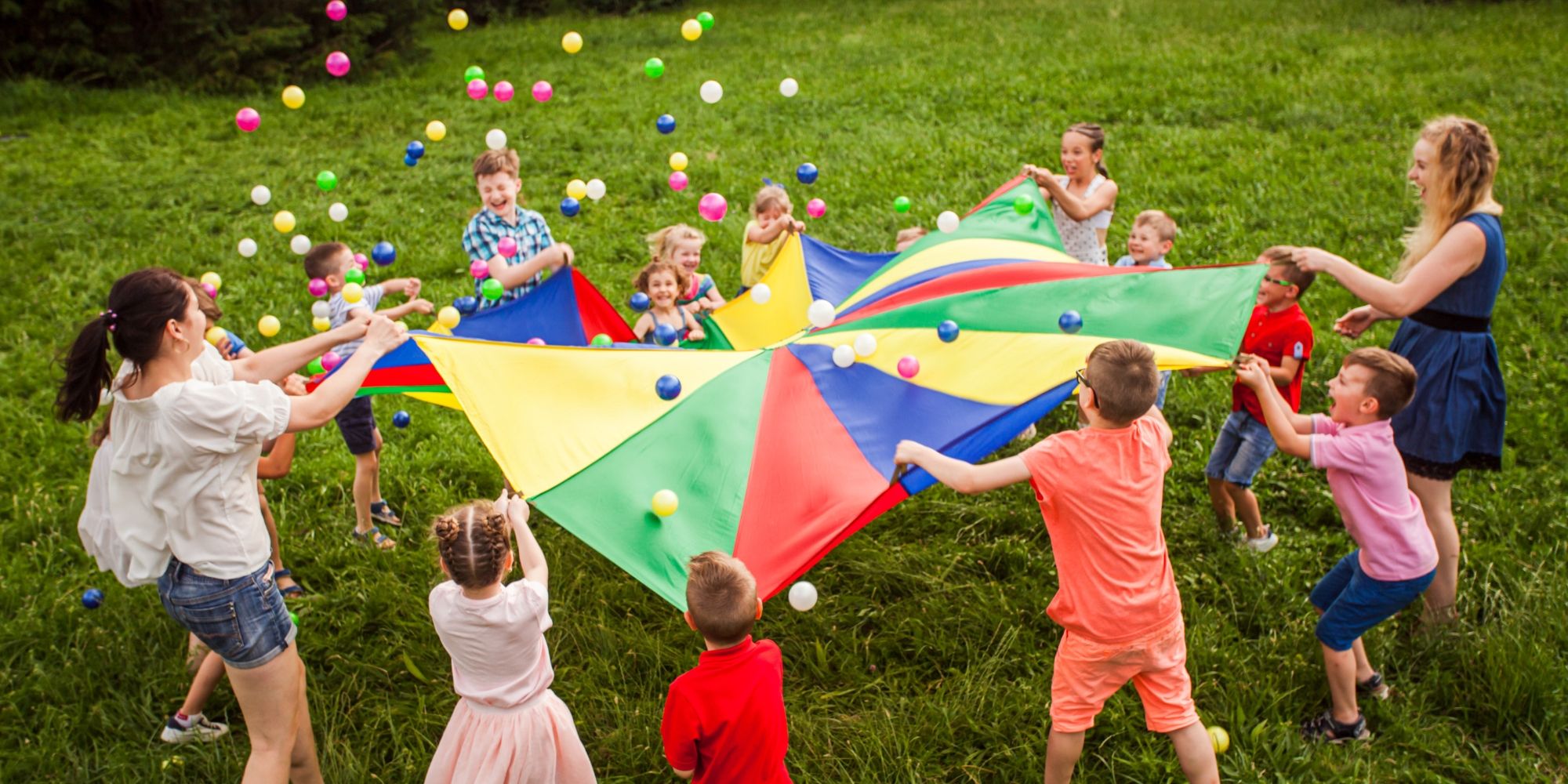 Parents and children play together with a colorful parachute in a park.