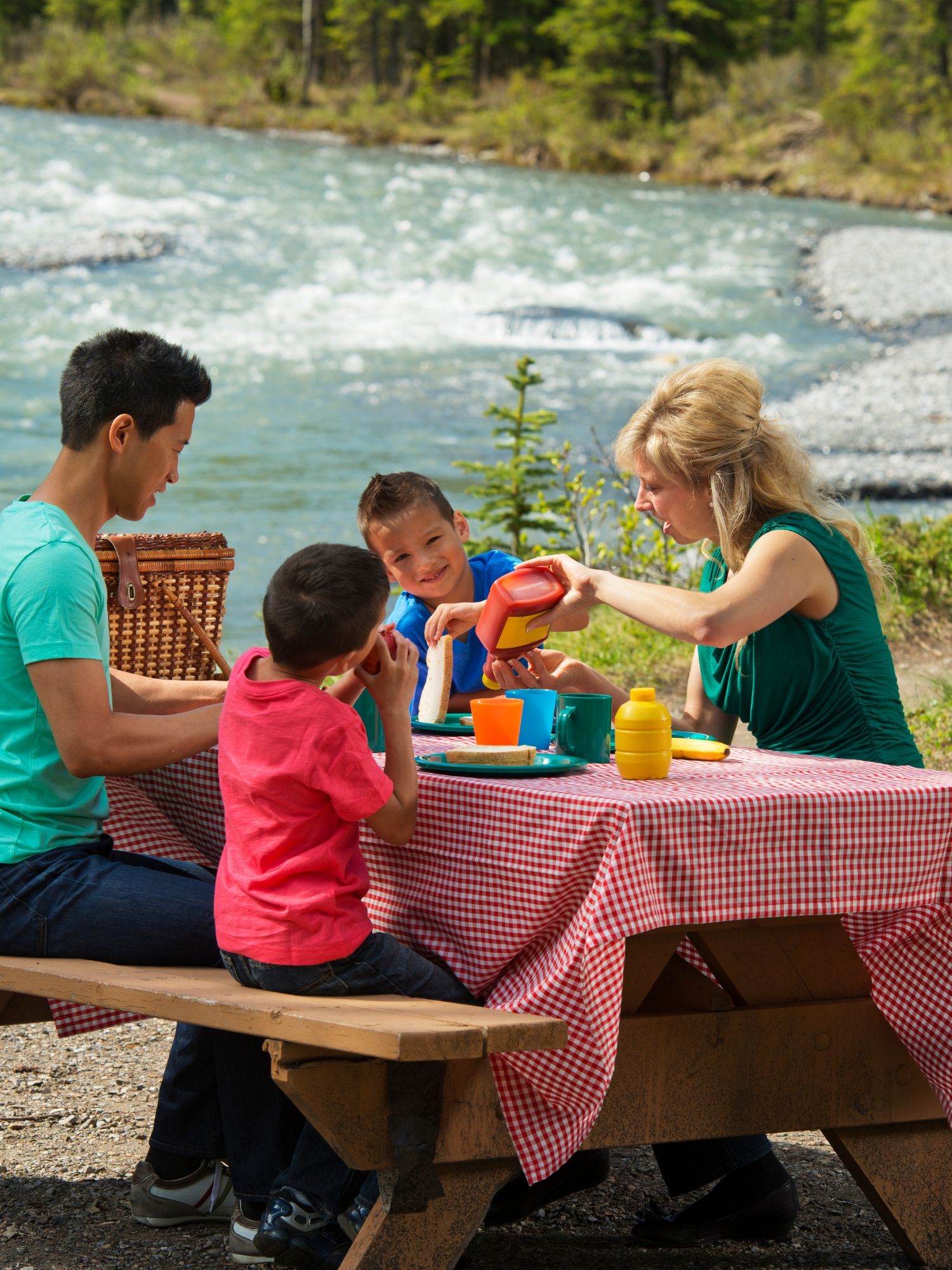 A family enjoys a picnic at a table beside a river.