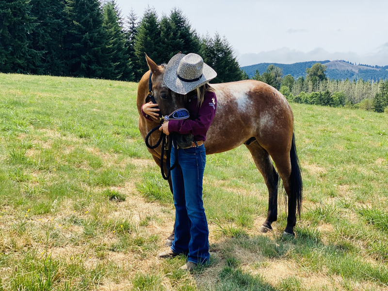 Woman in a cowboy hat embracing a horse in a green pasture
