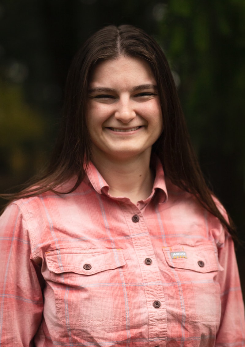 Headshot of a smiling woman wearing a pink plaid shirt