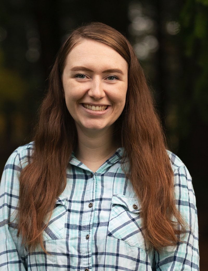 A smiling woman with long brown hair wearing a plaid shirt