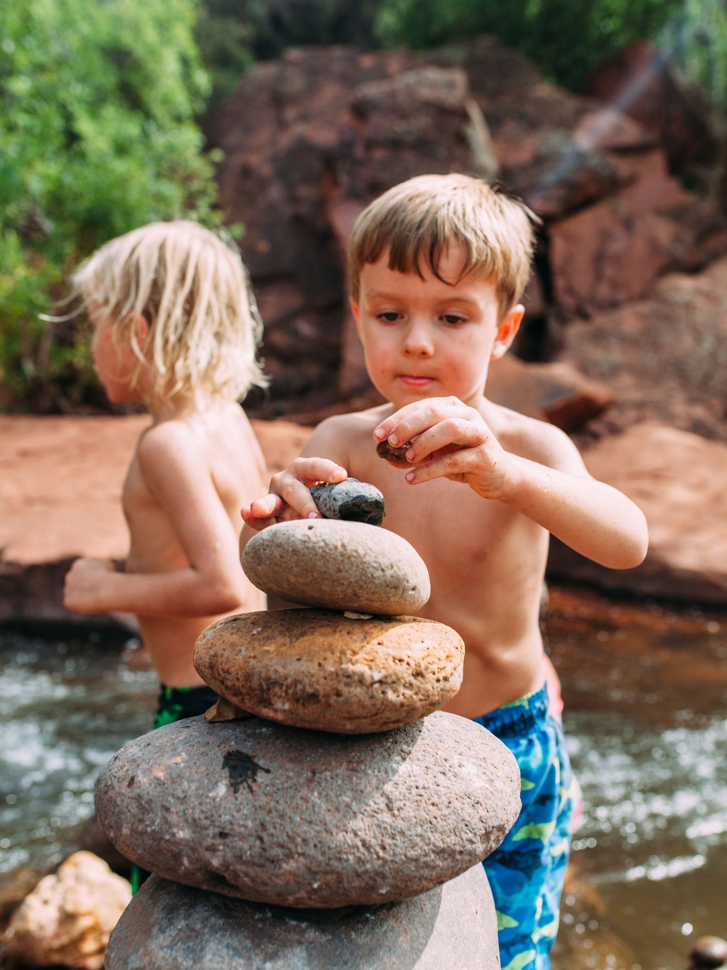 Children stack smooth rocks beside a river.