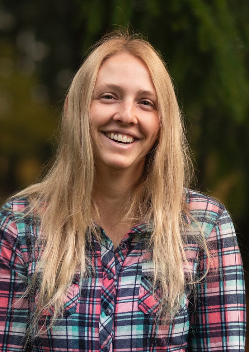 A smiling woman with long blonde hair wearing a plaid shirt