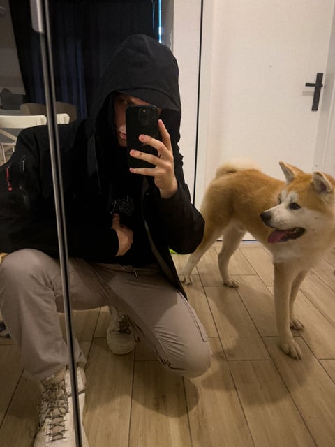 Man clothed in windbreaker, cargo pants and military-like white boots with a dog, Gen the Japanese Akita standing next to the mirror getting ready for the cold weather outside walkking